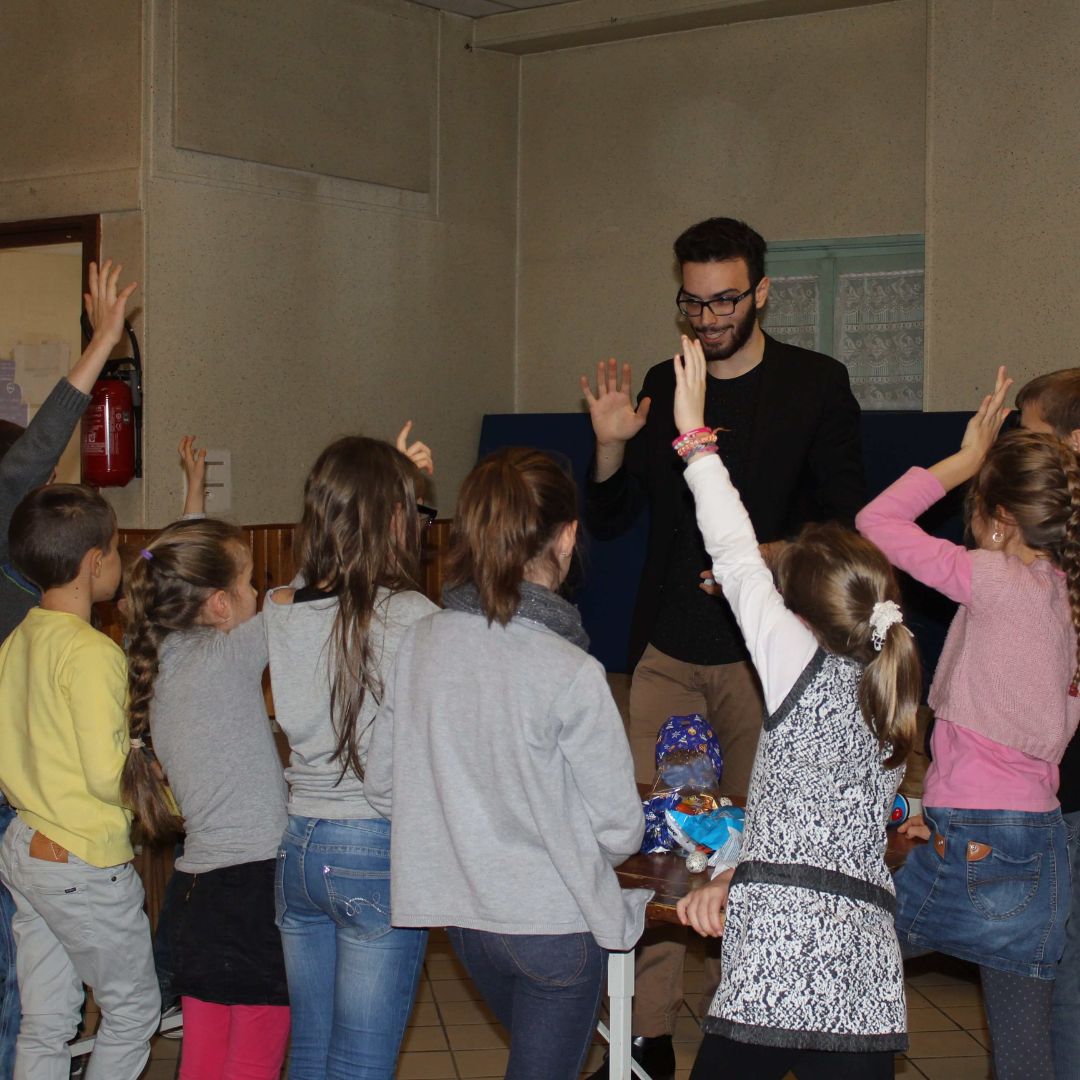 Sébastien devant un groupe d'enfant qui lève la main 