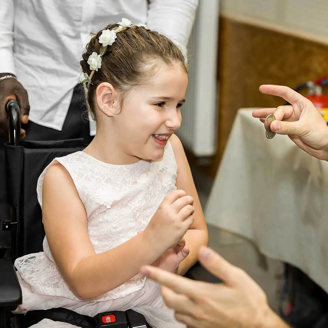 Une enfant dans un fauteuil roulant assiste à des tours de magie