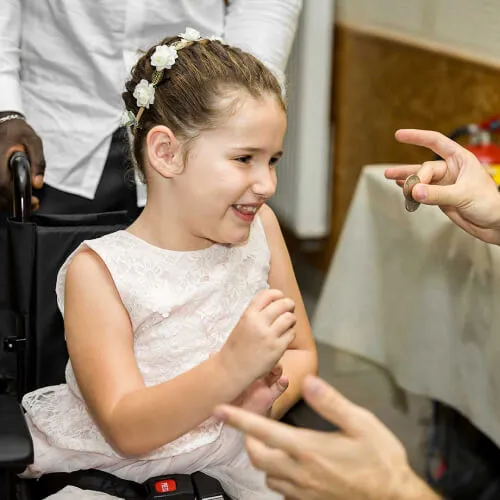Une enfant dans un fauteuil roulant assiste à des tours de magie